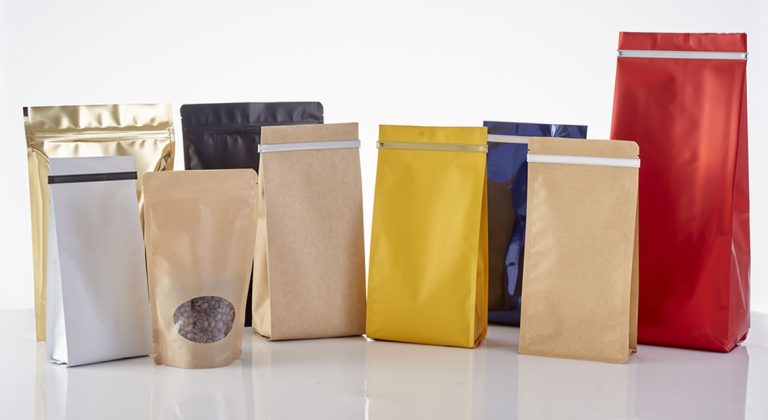 A colorful array of stand-up pouches, including kraft, gold, red, and blue, displayed on a glossy white surface.