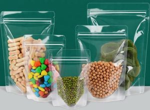 A variety of foods are displayed in clear, resealable bags against a green background.